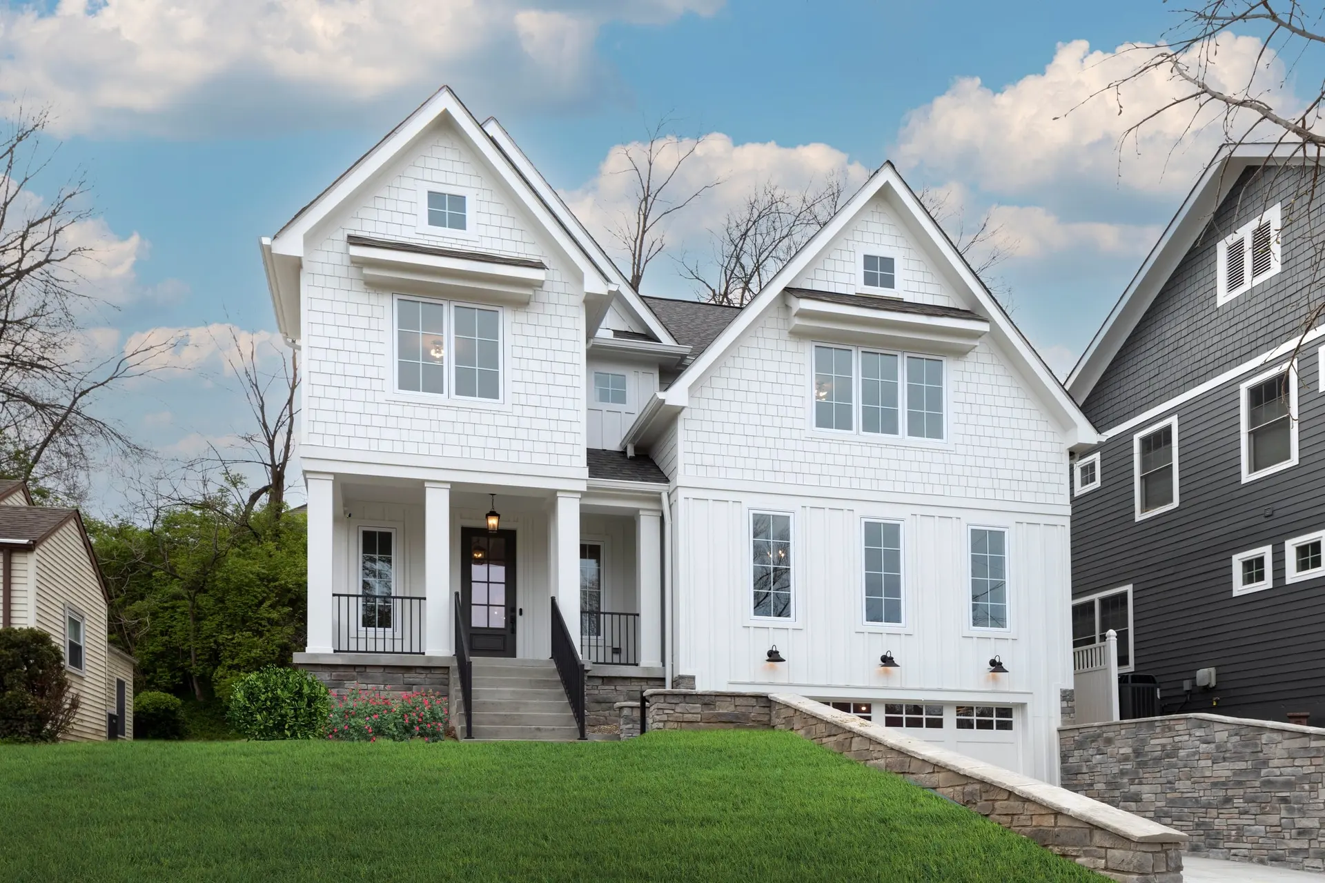 3399 Aultview in Mt. Lookout: a tall white farmhouse with two steep gables, black windows and a small front porch above a stone retaining wall